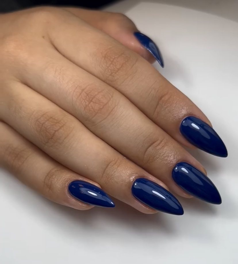 Handen met glanzende donkerblauwe almond-vormige nagels, gezet bij Glam & Glow Studio