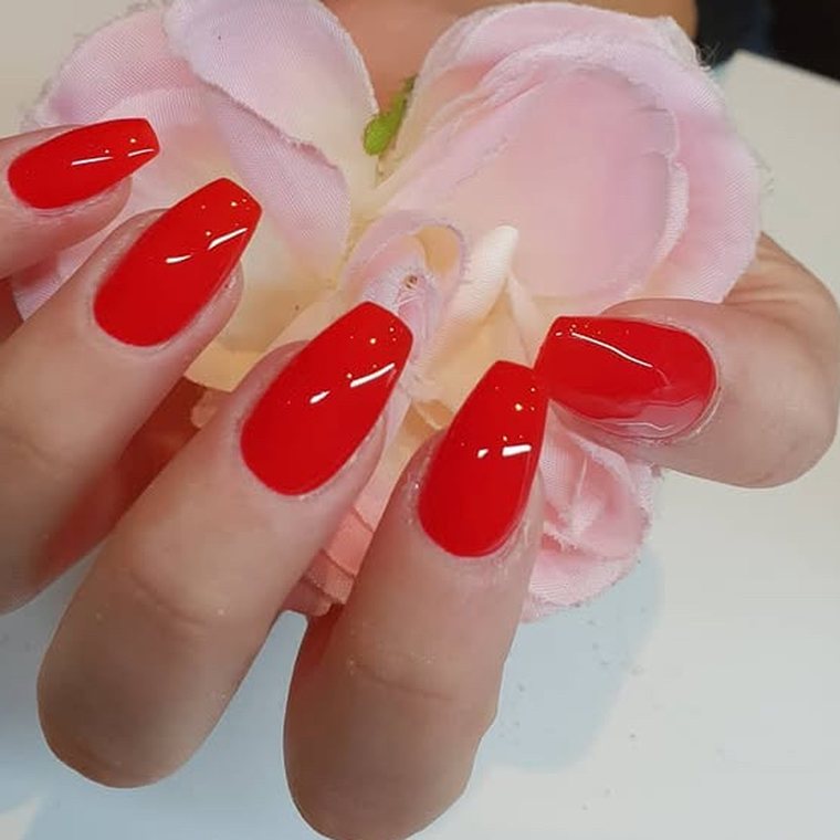 Felrode coffin-nagels bij een lichtroze bloem